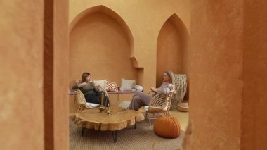 İki kadın, şık mobilyalarla bezenmiş sıcak renkli bir yaşam alanında dostça bir sohbeti paylaşıyor. Atmosfer davetkar ve rahat. Bağlanmak için mükemmel..