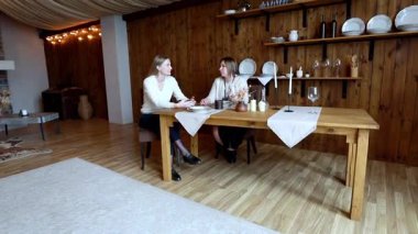 İki arkadaş, şık dekorasyonlarla süslenmiş sıcak ışıklı bir odada, ahşap bir masada oturuyor. Birbirlerine eşlik ederken derin sohbete dalarlar ve sıcak bir atmosferde eğlenirler..