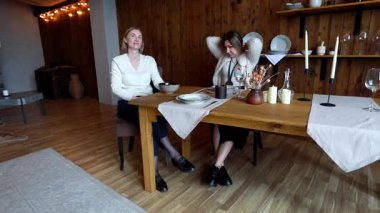 İki arkadaş, güzel bir ahşap masada oturmuş, kırsal cazibe ve yumuşak ışıklıklarla dolu sıcak ve davetkar bir mekanda sıcak bir yemeğin tadını çıkarırken, keyifli bir sohbeti paylaşıyor..