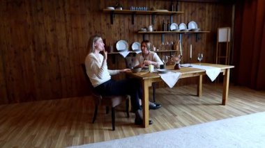 İki kadın sıcacık bir iç mekanda, zarif sofra takımlarıyla süslenmiş, ahşap bir masada sıcak bir sohbete girişiyor. Kahkahaları odayı dolduruyor..