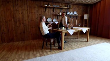 İki kadın, ahşap dekorla süslenmiş sıcak bir yemek salonunda sıcak bir toplantının tadını çıkarıyor. İyi hazırlanmış bir masada otururken gülücüklerini paylaşıyorlar ve hoş sohbetler ediyorlar..