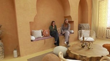 İki arkadaş, doğal dokular ve sıcak tonlarla dolu güzel tasarlanmış bir iç mekanda rahatça otururlar. Ortam rahat ve davetkar, sohbet ve rahatlama için mükemmel..