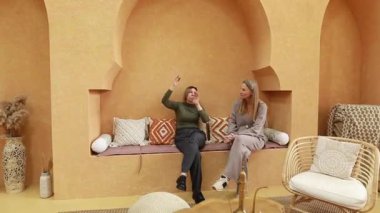 İki kişi en son tasarım eğilimlerini tartışırken, sıcak tonların ve tekstil aksanlarının yer aldığı şık, minimalist bir iç mekanda oturuyorlar. Atmosfer davetkar ve rahat..