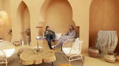 Kadınlar sıcak renkler ve minimalist mobilyalarla süslenmiş şık bir yaşam alanında huzurlu ve davetkar bir atmosfer sergileyen canlı bir sohbete girişir..