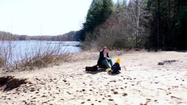 Bir kadın ve küçük çocuğu güneşli bir günü huzurlu bir gölün kumlu sahilinde geçirirler. Doğanın ve ilkbaharın başlarındaki temiz havanın tadını çıkarıyorlar..