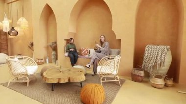 İki arkadaş rahat bir salonda, doğal dekorasyon ve dünyevi tonlarla çevrili bir şekilde rahatlar. Canlı bir sohbete dalarlar, davetkar bir ortamda birbirlerine eşlik ederek eğlenirler..