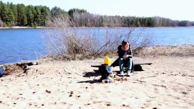 Aileler güneşli bir bahar günü göl kenarındaki kumlu bir plajda toplanırlar. Çocuklar kumda oynarken, yetişkinler rahatlar ve huzurlu manzaranın ve sıcak havanın tadını çıkarırlar..