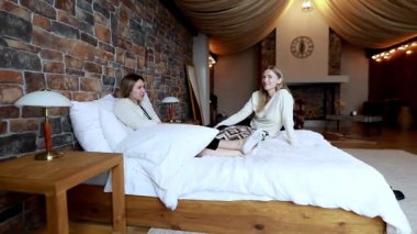 İki arkadaş, sıcak dekore edilmiş bir yerde rahat bir yatakta uzanırken aynı neşeli sohbeti paylaşıyor. Davetkar köy ortamı bir sakinlik ve bağ hissi uyandırıyor..