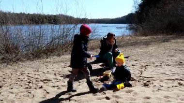 Güneşli bir günde, iki çocuk kumsalda oynaşmaktan zevk alırken anneleri yakınlarda oturup, bu sakin açık havada onları seyrediyor ve onlarla meşgul oluyor..