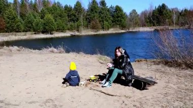 Bir anne ve küçük çocuğu sakin bir gölde, kumlarda oynayarak ve güneşin sıcaklığının tadını çıkararak kaliteli zaman geçirirler. Çevredeki yeşillik neşe dolu deneyimlerini arttırır..