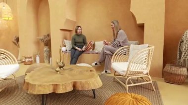 İki kadın, dünyevi renkler ve doğal malzemelerle süslenmiş sıcak, davetkar bir alanda dostça bir tartışmaya girişirler. Atmosfer konfor ve bağlantıyı teşvik eder.