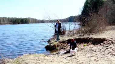 İki aile ferdi nehir kıyısında kaliteli zaman geçirir, biri olta atarken diğeri kumda oynar. Titreşimli ortam güneşli bir bahar gününü yansıtıyor..