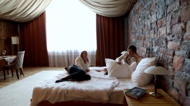 İki arkadaş, sıcak dekore edilmiş taş duvarlı bir odada sakin bir anın tadını çıkarıyor. Yumuşak ışık bir yatakta rahatça uzanırken süzülür, kahkahalar ve hikayeler paylaşır..