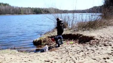 Çocuklar nehir kenarında güneşli bir günün tadını çıkarırken, bir köpek kumlu bölgeyi araştırırken dışarıda etkinlikler oluyor. Huzurlu ortam ağaçlar ve suyla çevrili..