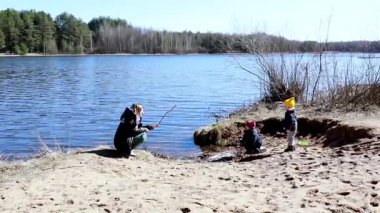 İki çocuk dışarıda sakin bir gölün yakınında oyun oynuyorlar, kumu kazıyorlar ve bir yetişkin yakından izlerken çubuk topluyorlar. Aydınlık gün, keşfi ve eğlenceyi davet eder.