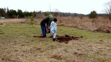 Aileler, genişleyen bir kırsal alana genç ağaçlar dikmek için bir araya gelirler. Çocuklar hevesle katılır, çukur kazar ve serin bir günde doğa hakkında bir şeyler öğrenirler..