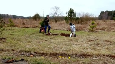 Bir ebeveyn ve çocuk kırsal bir alanda toprağı kazarak, bulutlar yükseldikçe tohum veya küçük ağaçlar ekerler. Soğuk hava sıcacık bahçıvanlık atmosferine ekleniyor..