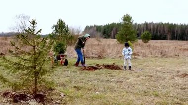 Bir aile, çukur kazıp zemin hazırlarken kırsal bir alanda ağaç dikme faaliyetlerine girişir. Bulutlu bir gün, dışarıda çalışmak için rahat bir atmosfer yaratıyor..