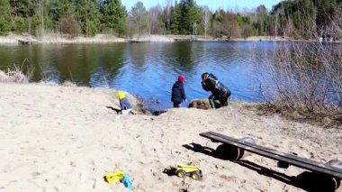 Bir aile güneşli bir günde göl kenarında vakit geçirir. Çocuklar kumda oynarken, yetişkinler yakınlarda dinlenip izliyorlar. Doğa onları ağaçlar ve sakin suyla çevreler..