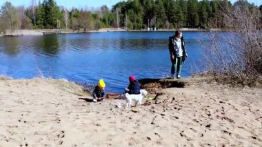 Aile sakin bir göl kenarında güneşli bir öğleden sonra geçirir. Çocuklar kumda oynarken bir köpek çevreyi keşfediyor. Etrafı doğa ile çevrili rahat bir atmosfer..