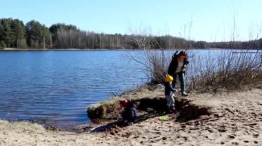 Bir aile ağaçlarla çevrili sakin bir göl kenarında vakit geçirir. Çocuklar kumlu sahili keşfetmek ve sıcak bir günde güzel havanın tadını çıkarmak için oyun oynuyorlar..