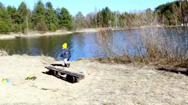 İki çocuk gölün kıyısındaki kumlu bir sahili renkli şapkalar giyerek keşfediyorlar. Güneş, ağaçlar ve doğa tarafından çevrelenmiş, suyun yanında oynarken parlıyor..