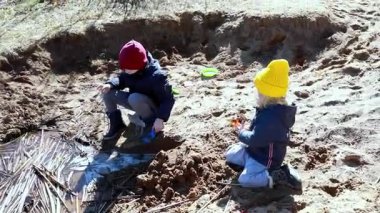 İki çocuk kumsalda eğlenceli keşifler yapar, kumları kazar ve açık havada güneşli bir günün tadını çıkarırken suyla etkileşime geçerler..