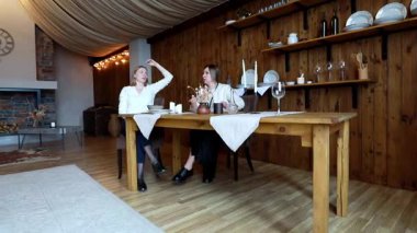 İki kadın sıcak, davetkar bir yerde, ahşap bir masada oturup sohbet ediyorlar. Sıcak atmosferde dekoratif aksanlar, hafif ışıklandırma ve kırsal bir cazibe var..