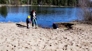 İki küçük çocuk kumlu sahili keşfederken, bir yetişkin de yakınlardan kumu kazıyor. Göl, bu güzel günde arka planda güneş ışığını yansıtır..