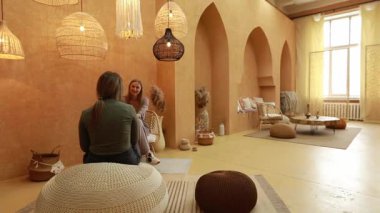 İki kadın, doğal malzemelerle süslenmiş sakin, minimalist bir odada rahatça oturuyorlar..