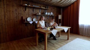 Ilık, ahşap bir odada iki birey birlikte yemek yiyor. Masada çok hoş bir düzenleme var. Vitrin gözlükleri, tabaklar ve bir süs eşyası..