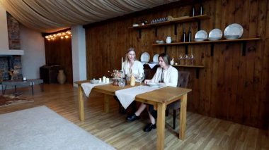 İki kişi güzel düzenlenmiş bir ahşap yemek masasında yemek hazırlığı yapıyor. Mumlar ve dekoratif eşyalar odanın rahat atmosferini arttırır..