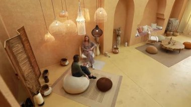 İki insan doğal dekor ve yumuşak ışıklandırmayla dolu ılık bir iç mekanda sohbet ediyorlar. Çevre rahatlama ve rahatlamaya davet eder, sosyal toplantılar için mükemmeldir..