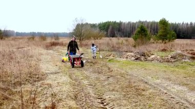 İki birey kırsal alanda bahçe ve peyzaj işleriyle uğraşır. Biri el arabası kullanırken diğeri toprağı ekme ya da kazma üzerinde çalışıyor. Kırsalda ilkbahar..