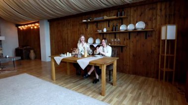 İki arkadaş, ahşap bir masada mumlar ve çiçeklerle süslenmiş, rahat, kırsal bir odada oturuyor. Sohbete dalarlar, sıcak ve davetkar bir ortam yaratırlar. Yemek için mükemmel..