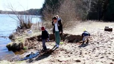 Çocuklar sakin bir gölün kumlu sahilinde, bir yetişkin nezaret ederken eğlenceli aktivitelere girişiyor. Sıcak güneş ve doğal güzellik keşif ve eğlence günlerini daha da güzelleştirir..