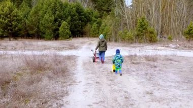 Bir anne ve çocuğu ağaçlık bir alanda toprak bir patika boyunca yürürler. Çocuk mutlu bir şekilde bir vagon çeker, sakin bir manzarayı keşfeder..