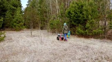 Aile üyeleri, ağaçlarla çevrili yemyeşil bir alanda bahçıvanlık yapmakla meşgul. Birlikte çalışıyorlar, manzarayı iyileştirmek için el arabası ve aletler kullanıyorlar..
