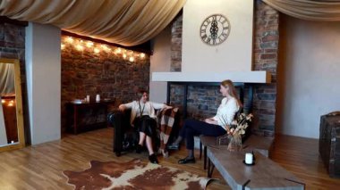 İki arkadaş, kırsal bir odada rahat bir şekilde otururken canlı bir sohbete girişiyor. Sıcak atmosfer, rahat dekor ve ortam aydınlatmasıyla güçlenir..