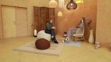 Ilık ışıklandırma ve doğal dekorla dolu rahat ve şık bir odada rahatça oturan iki kadın. Düşünceli bir tartışmaya girerek, içgörülerini ve hikayelerini paylaşıyorlar..