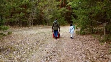Bir anne ve çocuğu erzak dolu bir vagon taşıyarak orman yolunda yürüyorlar. Çevrelerinde ağaçlar ve düşen yapraklar var. Huzurlu bir atmosfer yaratıyorlar..