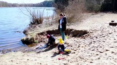 İki çocuk gölün kenarındaki kumda oynar, ilginç bir şekilde doğayı kazar ve keşfederken, bir yetişkin baharda güneşli bir günde yakından izler..