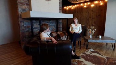 İki kadın rahat bir odada oturup rahatça sohbet ediyorlar. Sıcak atmosferde ahşap duvarlar, taş bir şömine ve davetkar bir ışıklandırma var. Tartışmaları dostane ve rahatlatıcı görünüyor..