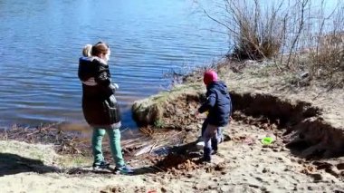 İki çocuk kumlu bir nehir kıyısında açık hava aktivitelerinin keyfini çıkarırken bir yetişkin gözetliyor. Bölgeyi keşfederler, çubuk toplarlar ve öğleden sonra güneşinde oyuncaklarla oynarlar..