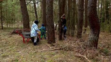 İki kişi ağaçlık bir alanda düşen dalları temizlemekle meşgul. Biri el arabası kullanırken, diğeri ağaçların dallarını kesiyor. Serin bir sonbahar günü, yemyeşil ağaçlarla çevrili..