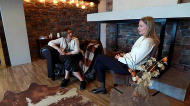 İki kadın büyüleyici bir salonda gevşeyip, hareketli bir sohbete dalıyorlar. Kurulumda taş duvarlar, rahat koltuklar ve hoş bir atmosfer yaratan hafif ışıklandırma yer alıyor..