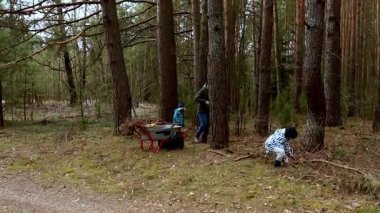 Aile üyeleri sakin bir ormanda çalıların temizlenmesi konusunda işbirliği yaparlar. Sahnede yetişkinler ve çocuklar, açık bir gökyüzünün altındaki yüksek ağaçların arasından enkazı dikkatlice kaldırıyorlar..