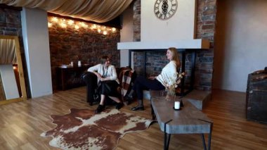 İki kadın modern ama kırsal bir oturma odasında otururken neşeli bir sohbete girişiyor. Uzay sıcak bir atmosfere ve sıcak bir şömineye sahiptir..