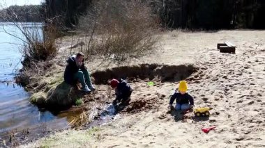 Çocuklar göl kenarındaki kumda kazıp oynuyorlar. Yetişkinler yakınlarda dinleniyor, sıcak güneşin ve huzurlu çevrenin tadını çıkarıyor, harika anılar yaratıyorlar..