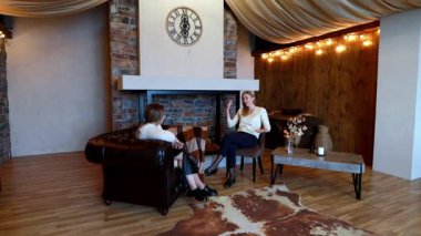 Sıcak ve davetkar bir odada, iki kadın şık mobilyaların üzerinde rahatça otururken anlamlı bir konuşma yapıyorlar. Atmosferde yumuşak ışıklandırma ve kırsal elementler var.